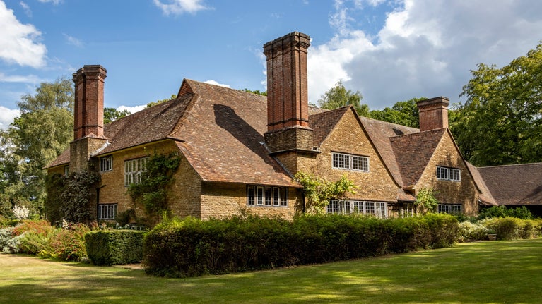 A large yellow stone house is pictured with three tall chimneys and a large tiled roof